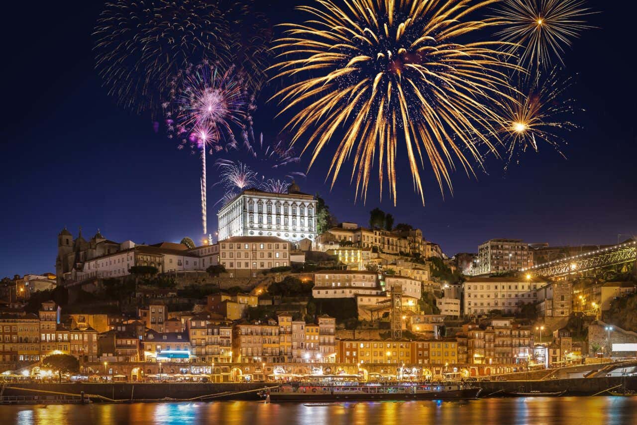 La città di Porto fotografata dal fiume Douro di sera mentre nel cielo esplodono i fuchi d'artificio
