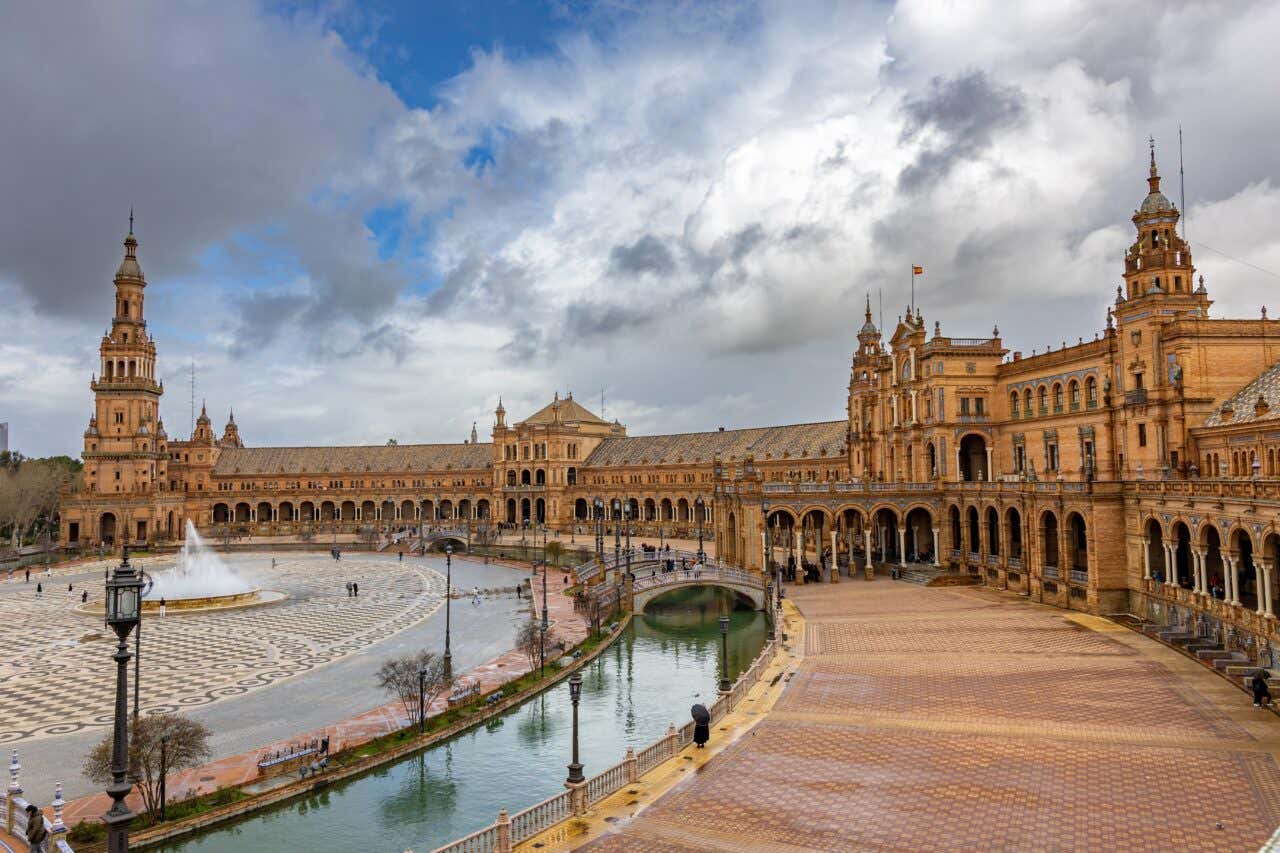 Plaza de España a Siviglia con l'edificio semicircolare in stile rinascimentale, il canale con ponti decorati e la pavimentazione a mosaico sotto un cielo nuvoloso