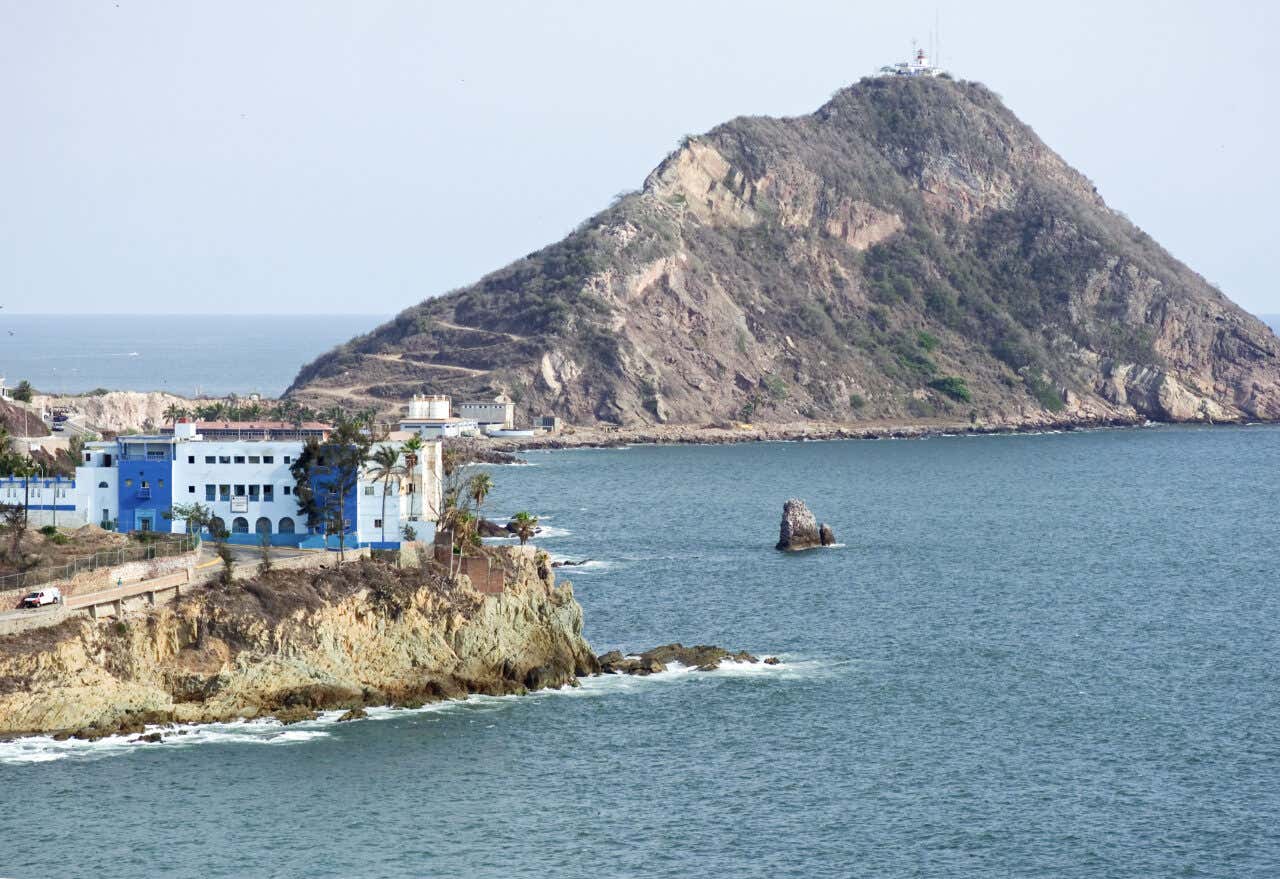El Faro de Mazatlán seen in the distance on the peninsula on an overcast day.