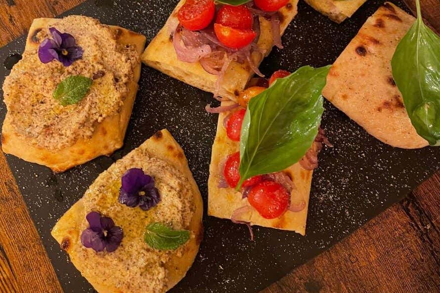 A view of flatbreads with various toppings on a black board on a wooden table.