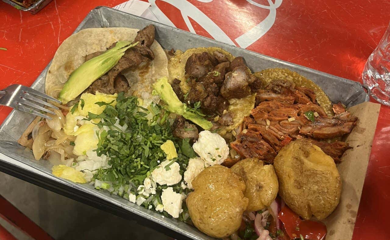 3 different tacos in the Taquería Orinoco, with avocado, cilantro, cheese, and potatoes on the side.