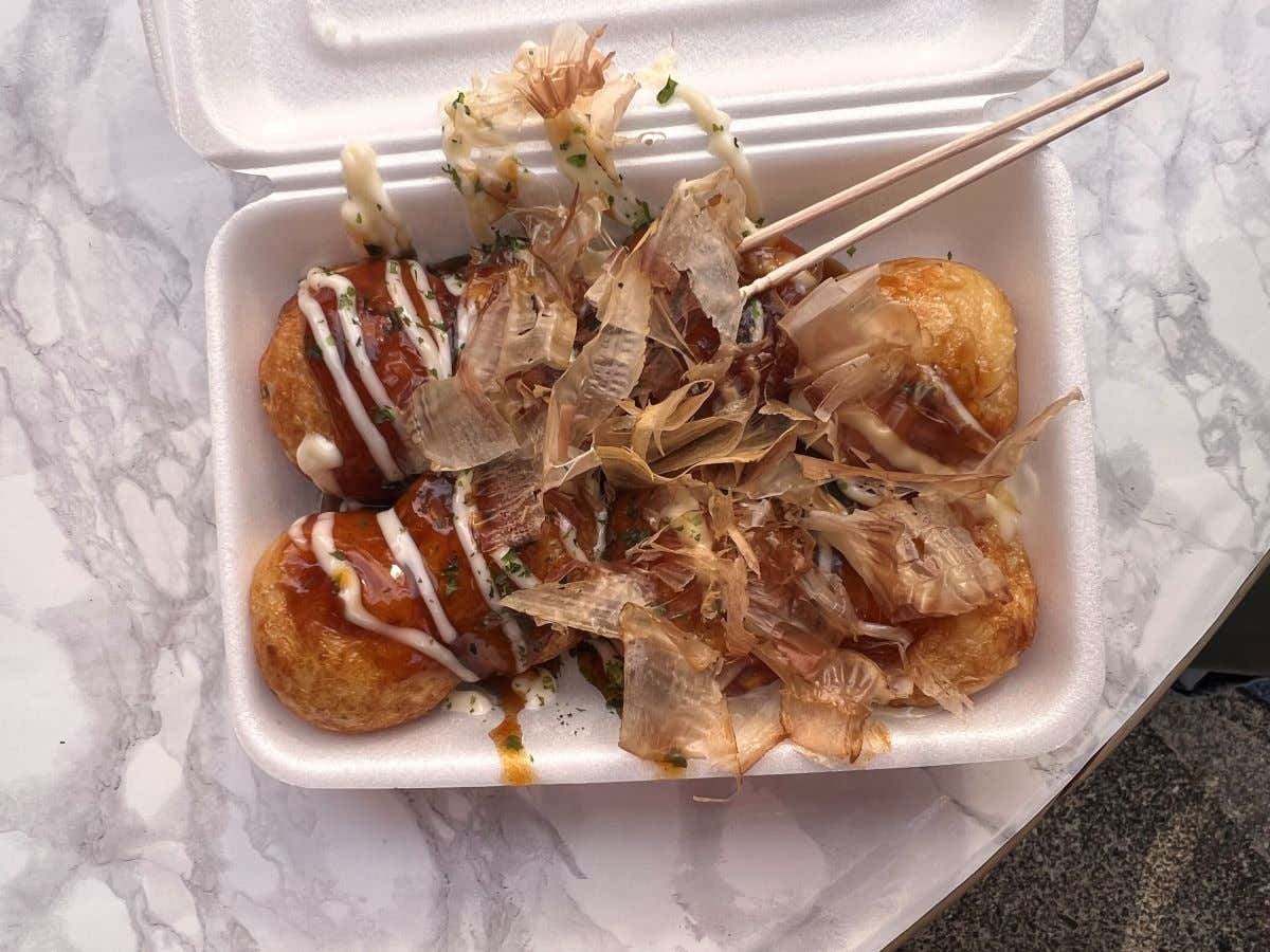 Detalle de un plato para llevar con takoyaki cubiertos de salsa