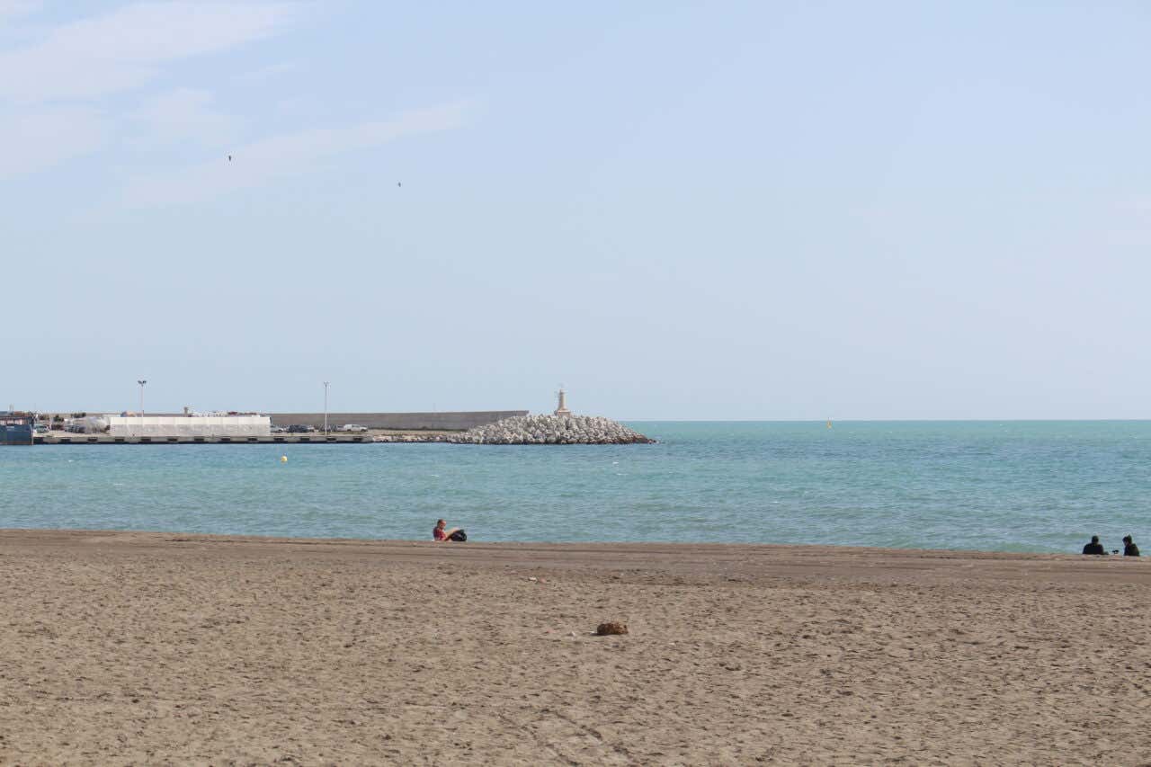 The calm beach of Málaga with the lighthouse in the distance
