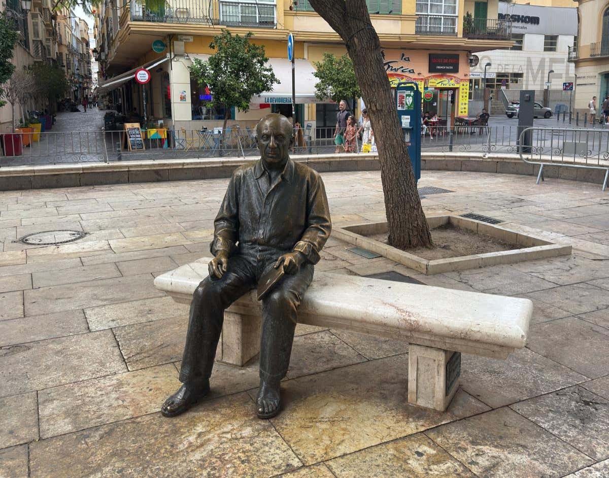 A bronze statue of Pablo Picasso sitting on a bench in a square in Málaga