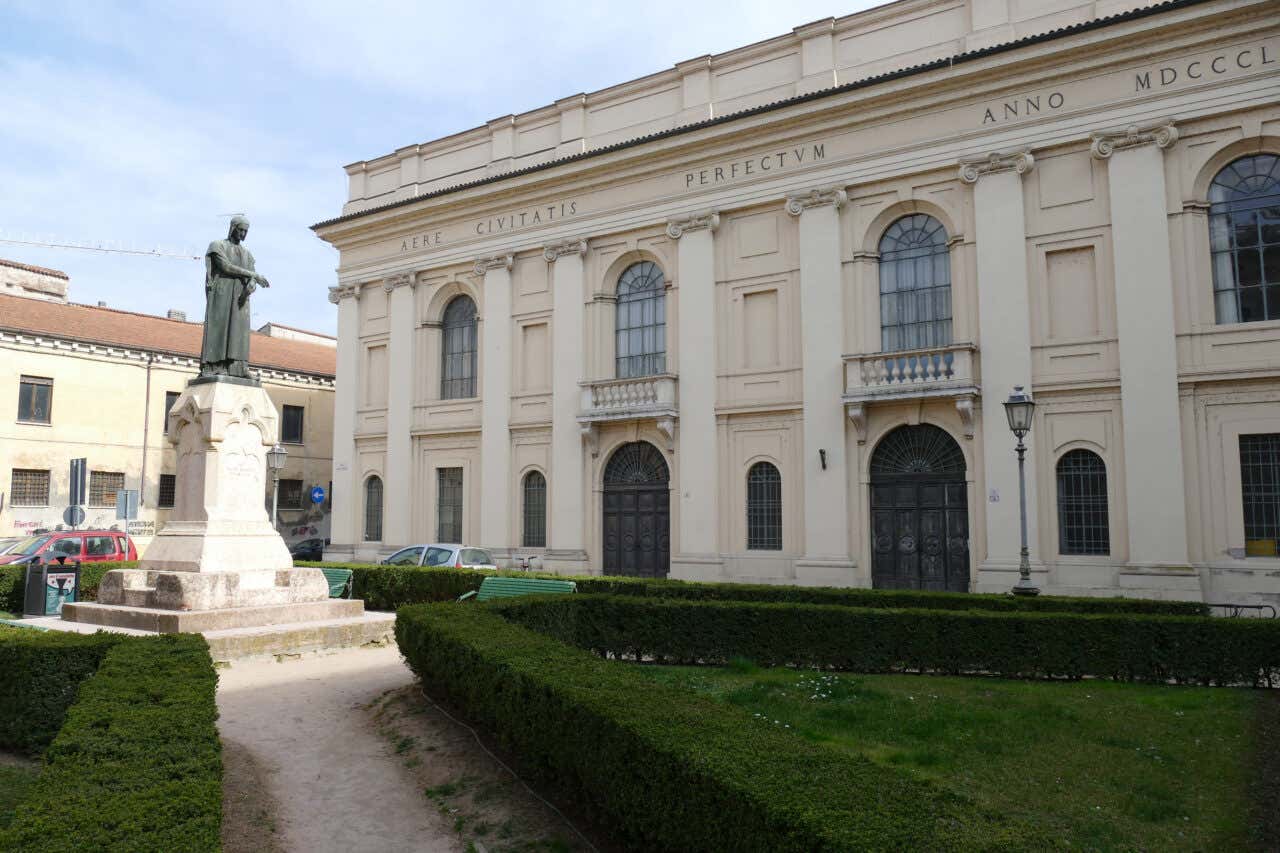 Facciata neoclassica del Teatro Bibiena a Mantova, con il giardino curato in primo piano e una statua su piedistallo al centro del giardino