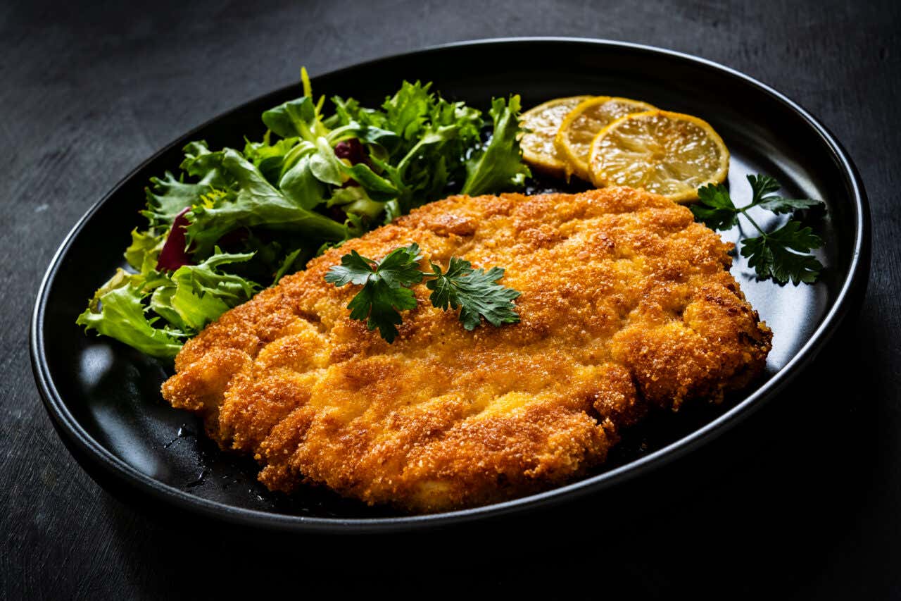 Carne empanada com uma salada de folhas verdes e fatias de limão em um prato preto