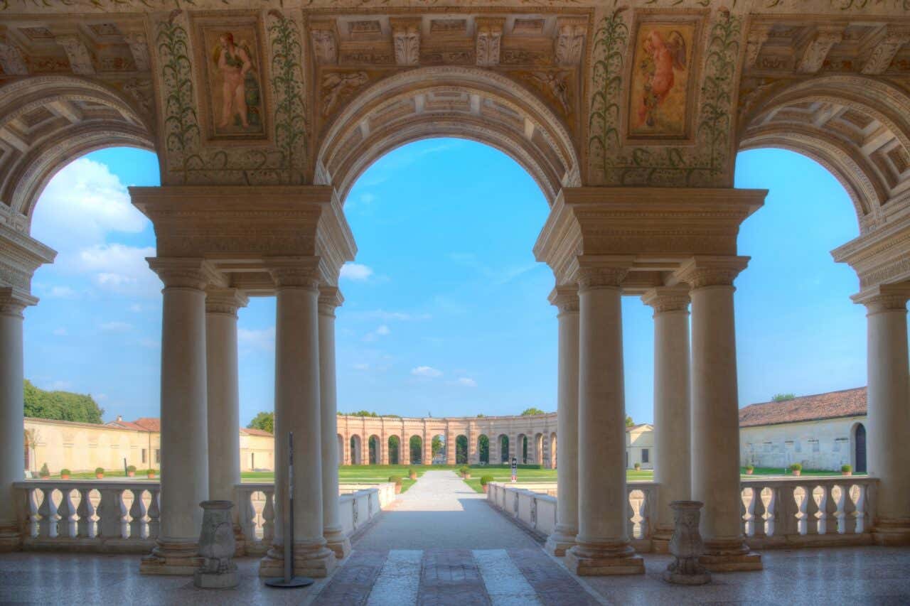 Loggiato di Palazzo Te a Mantova con colonne, archi decorati e vista sui giardini e cortile d'onore