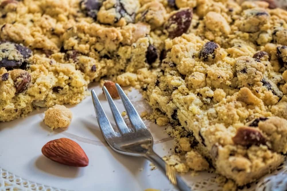 Una forchetta a tre denti in metallo poggiata su un piatto con un dolce fatto con farina di mandorle e mandorle intere