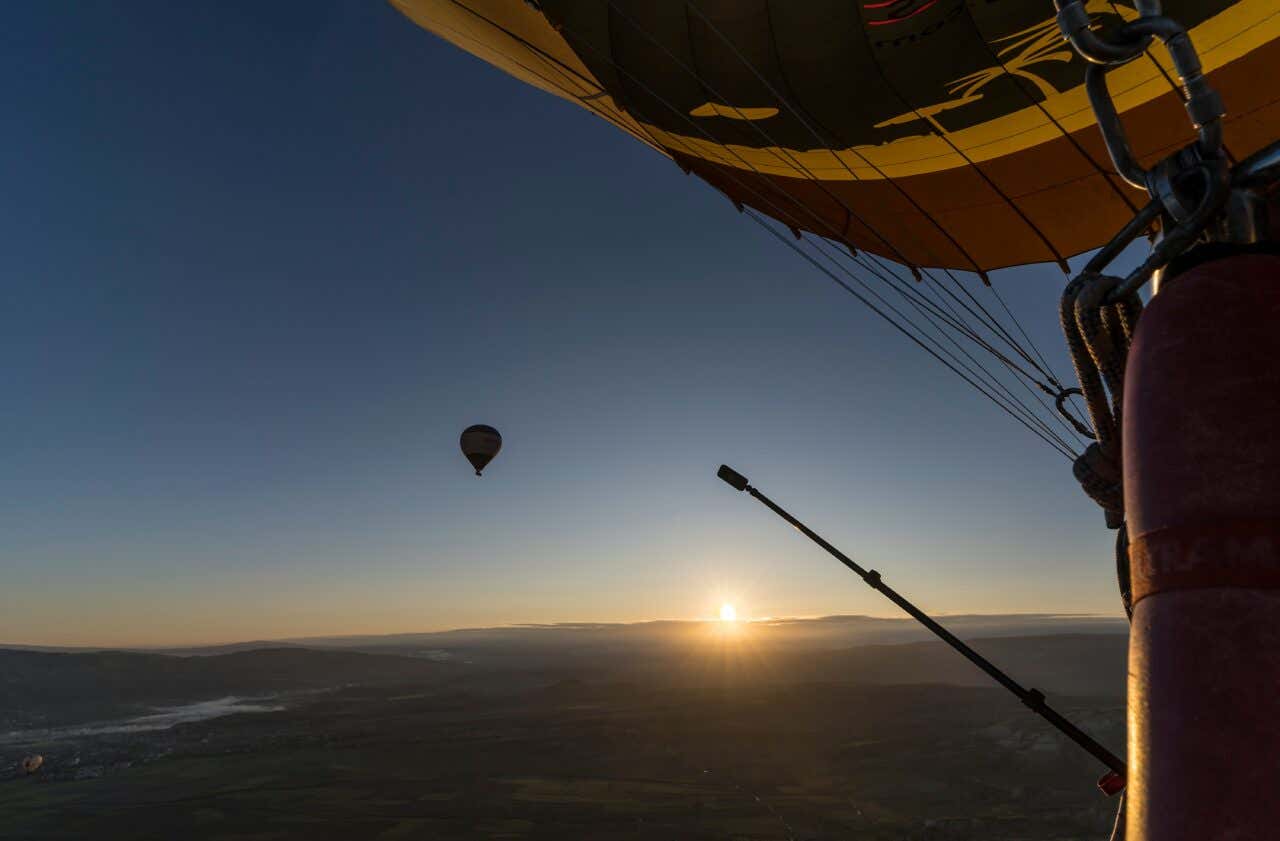 Capadocia as seen from a hot air balloon in the early morning, with a different hot air balloon in the background.