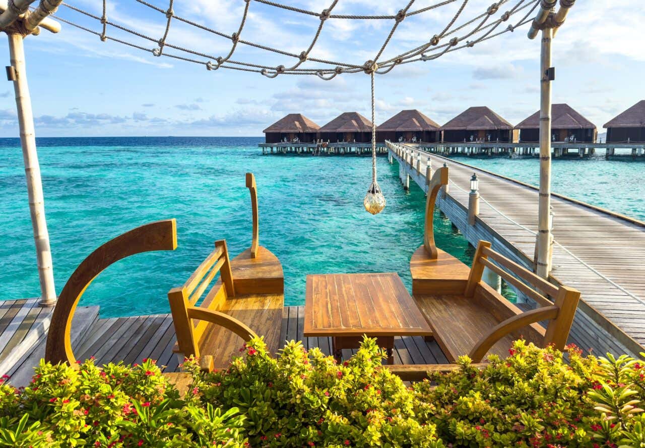 Uma mesa de madeira com bancos à beira-mar com bangalôs ao fundo