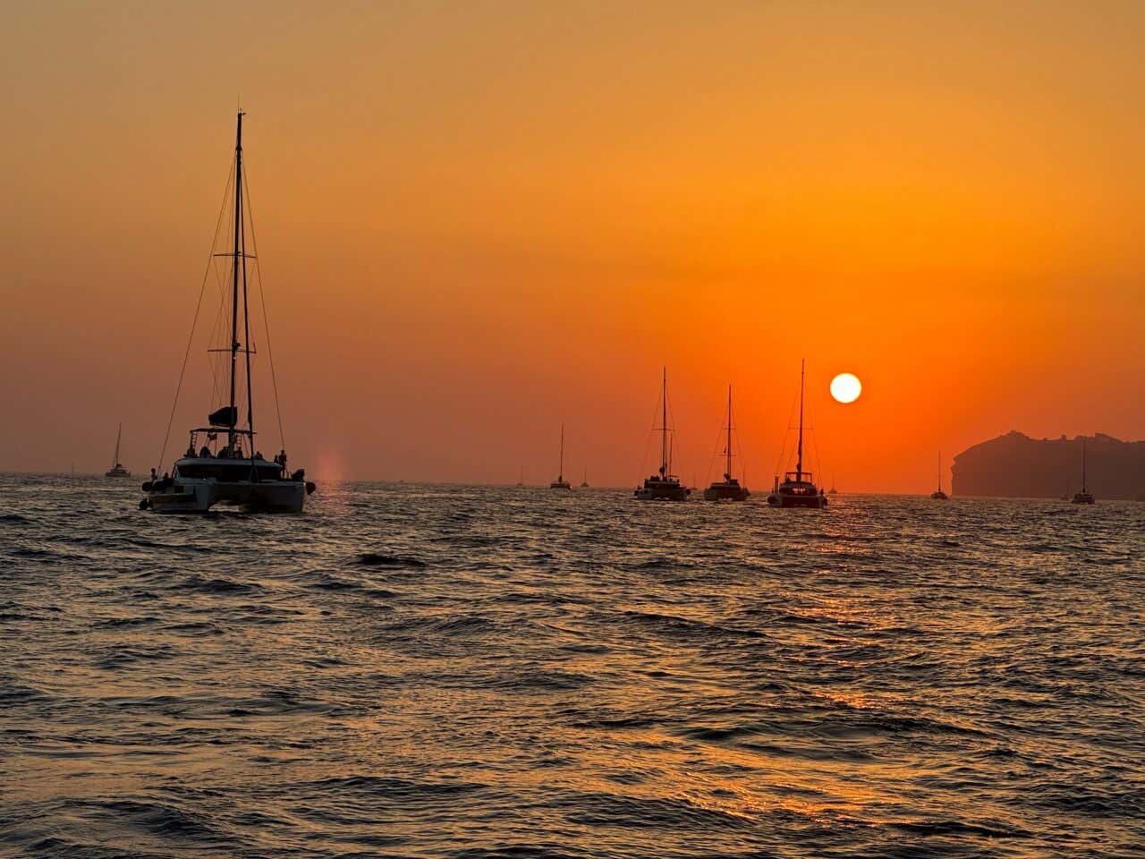 A bunch of boats sailing in the sea in Santorini as the sun sets.
