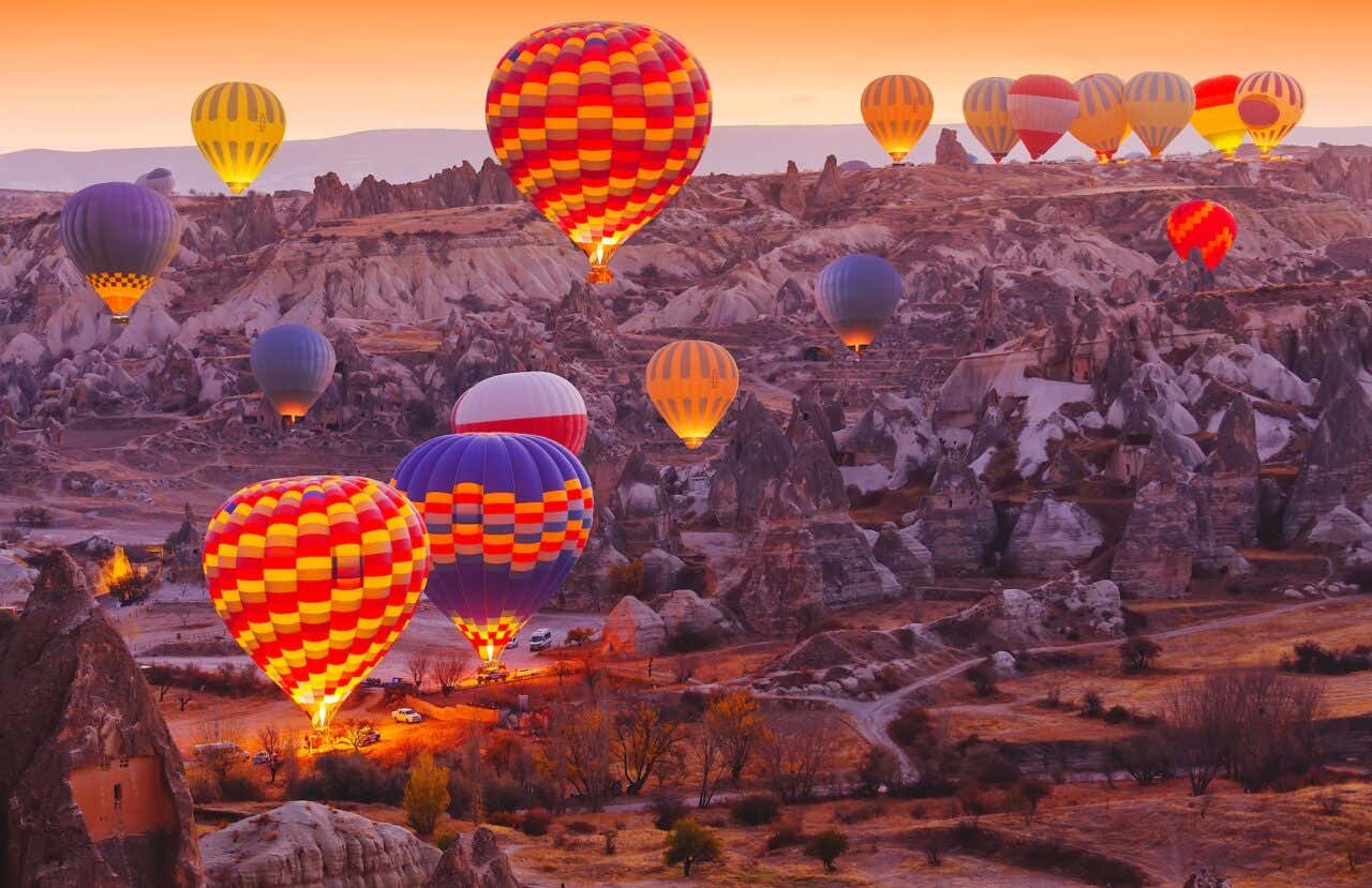 Balões coloridos levantando voo na paisagem característica da Capadócia ao nascer do sol