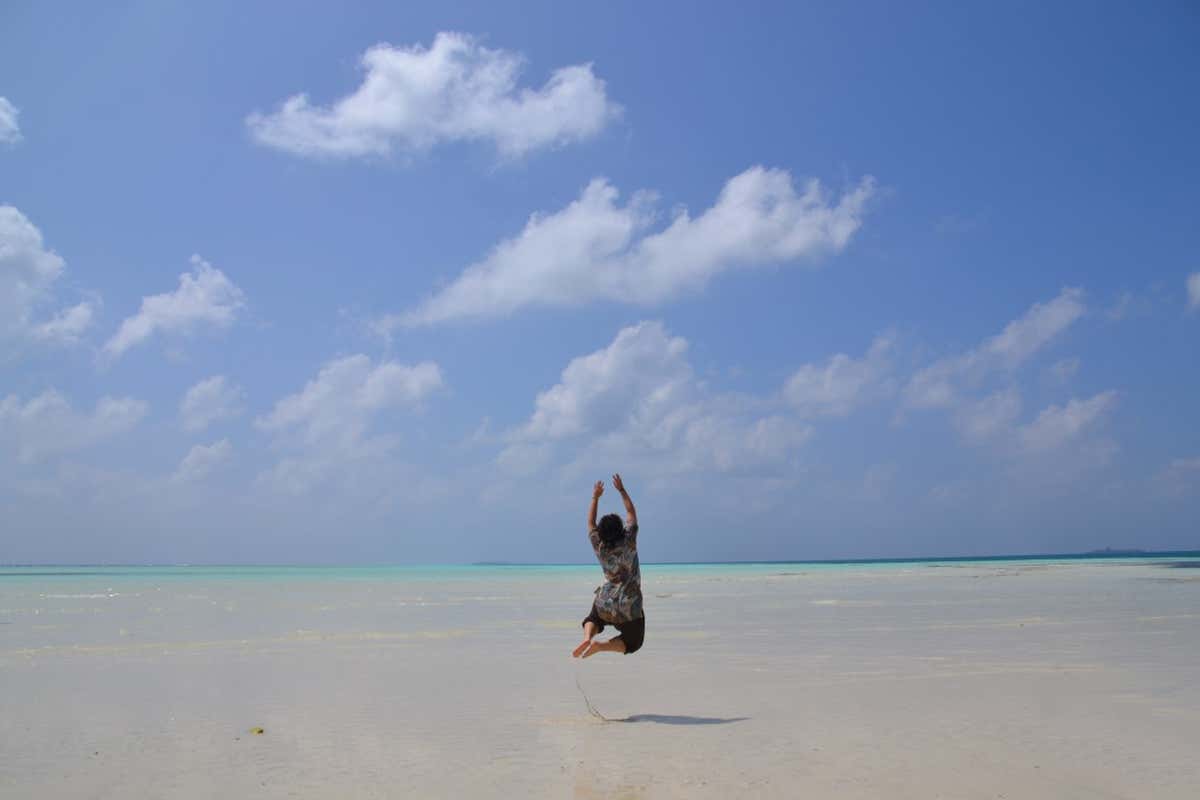 Mujer saltando en medio de una playa de arena blanca en Maldivas