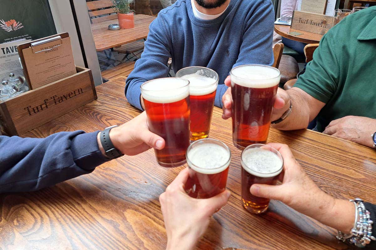 Cinco personas brindando con pintas de cerveza en una mesa de madera enTurf Tavern