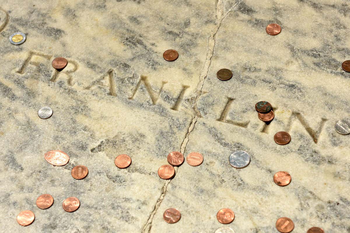 Monedas de dólares sobre la lápida de Benjamin Franklin