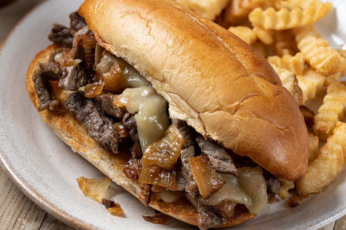 Un bocadillo de carne, cebolla y queso compañado de patatas