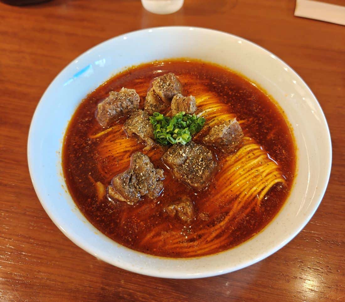 Detalle de un plato donde se ve un ramen con caldo rojizo y carne por encima