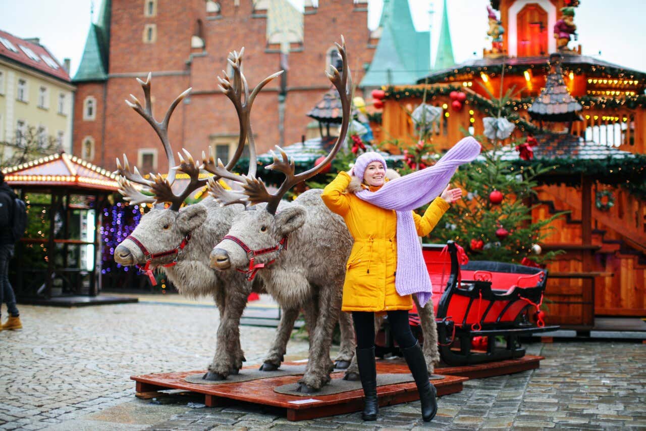 Uma mulher em um mercado natalino posando para uma foto com as decorações de duas renas.