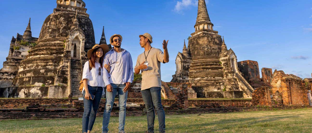 Una guida parla a due turisti davanti a dei templi in una giornata soleggiata