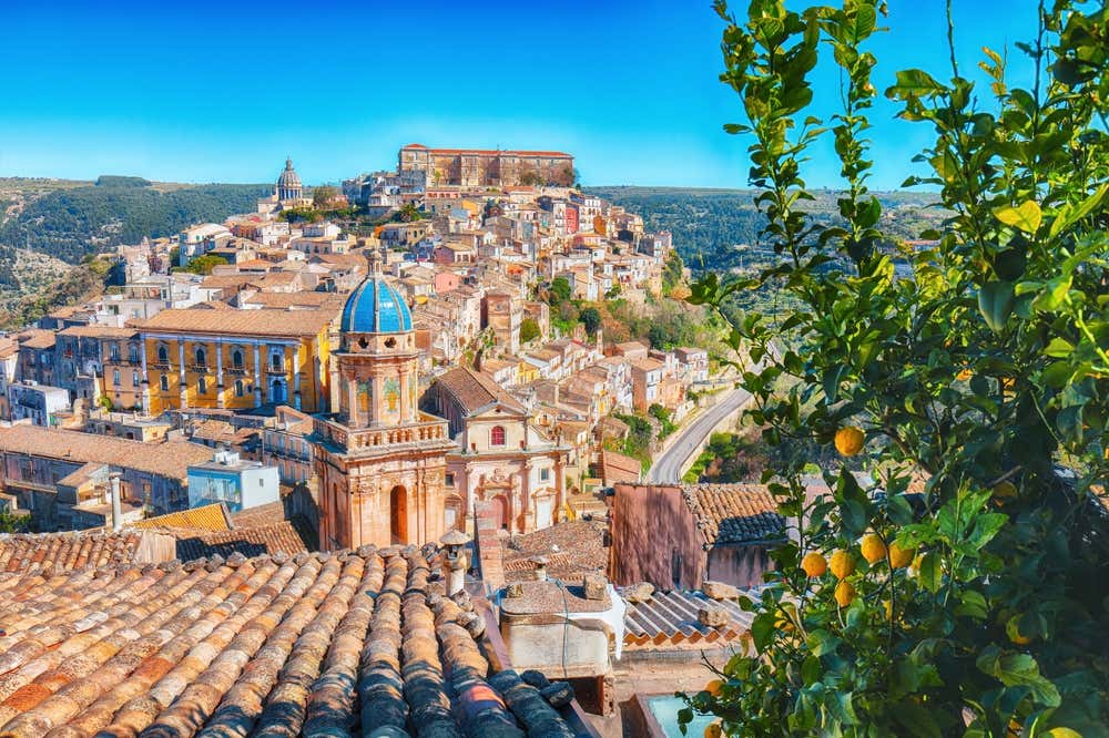 Vista panoramica di Noto, Sicilia, con architettura barocca, cupola blu, tetti in terracotta e alberi di agrumi in primo piano
