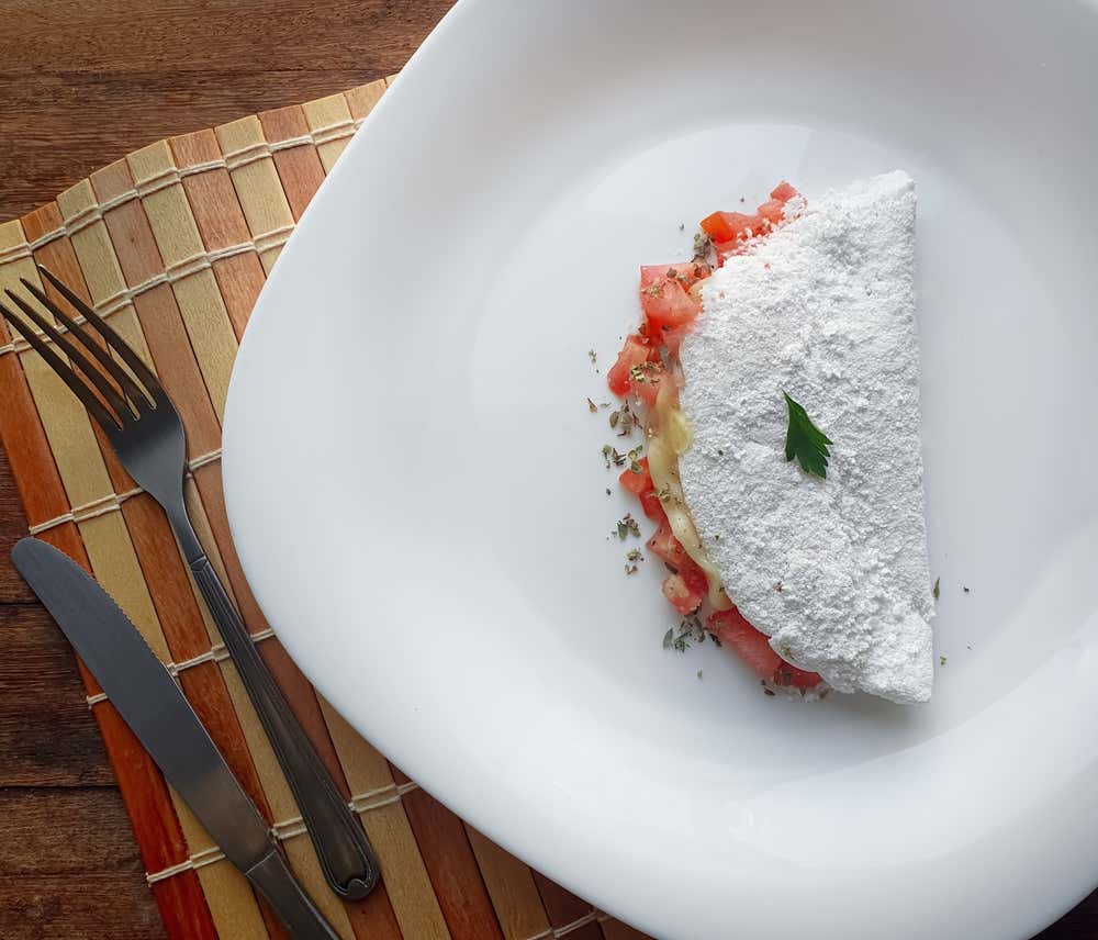 Tapioca com tomate, queijo e orégano em um prato branco