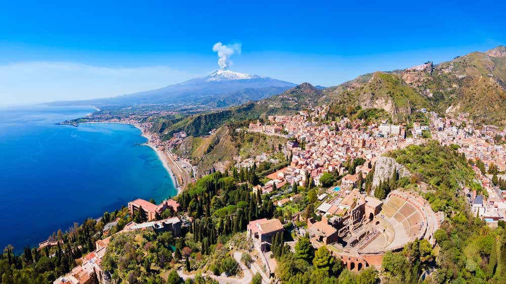 Il borgo di Taormina a picco sul mare con l'Etna che sbuffa sullo sfondo in lontananza