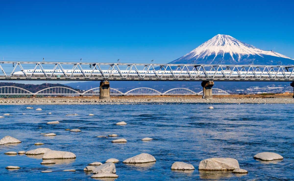 Tren bala pasando por un puente con el monte Fuji con nieve en su cumbre de fondo 