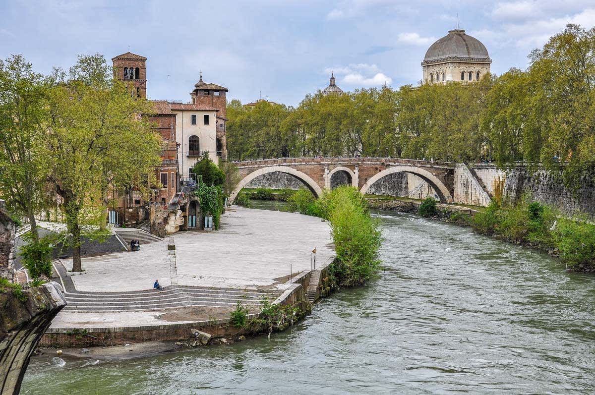 Vistas del río Tíber con un puente, edificios históricos y árboles.