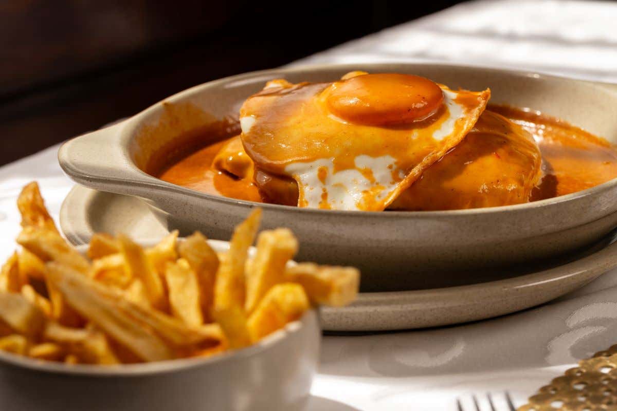 Mesa donde se ve un plato con una francesinha y unas patatas fritas