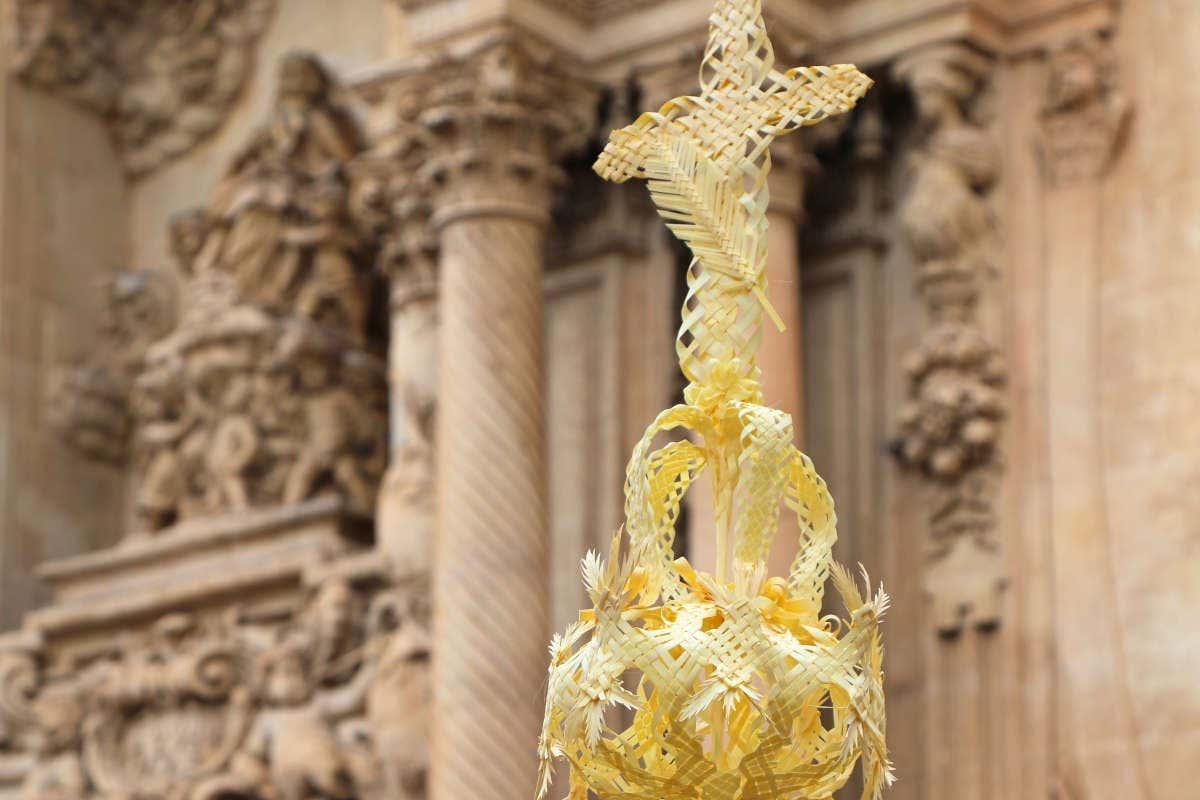 Una cruz hecha con hoja de palma amarilla delante de la fachada de una iglesia de la Comunitat Valenciana en Semana Santa