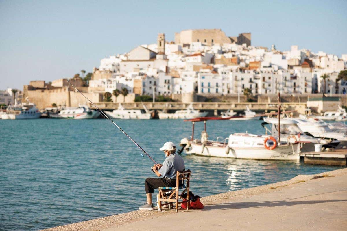 Un hombre mayor con gorra en una silla de madera pescando en Peñíscola