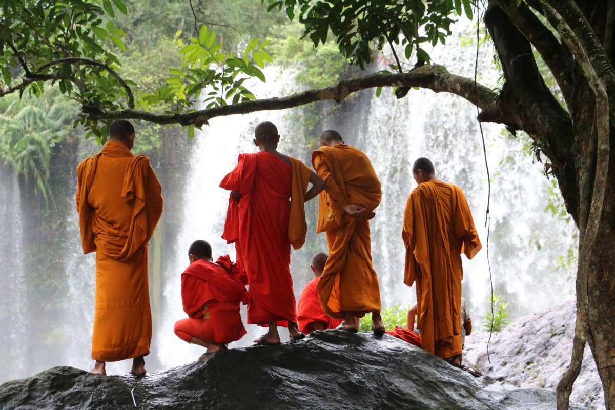 Moines vêtus de toges orange au bord d'une cascade à Phnom Kulen
