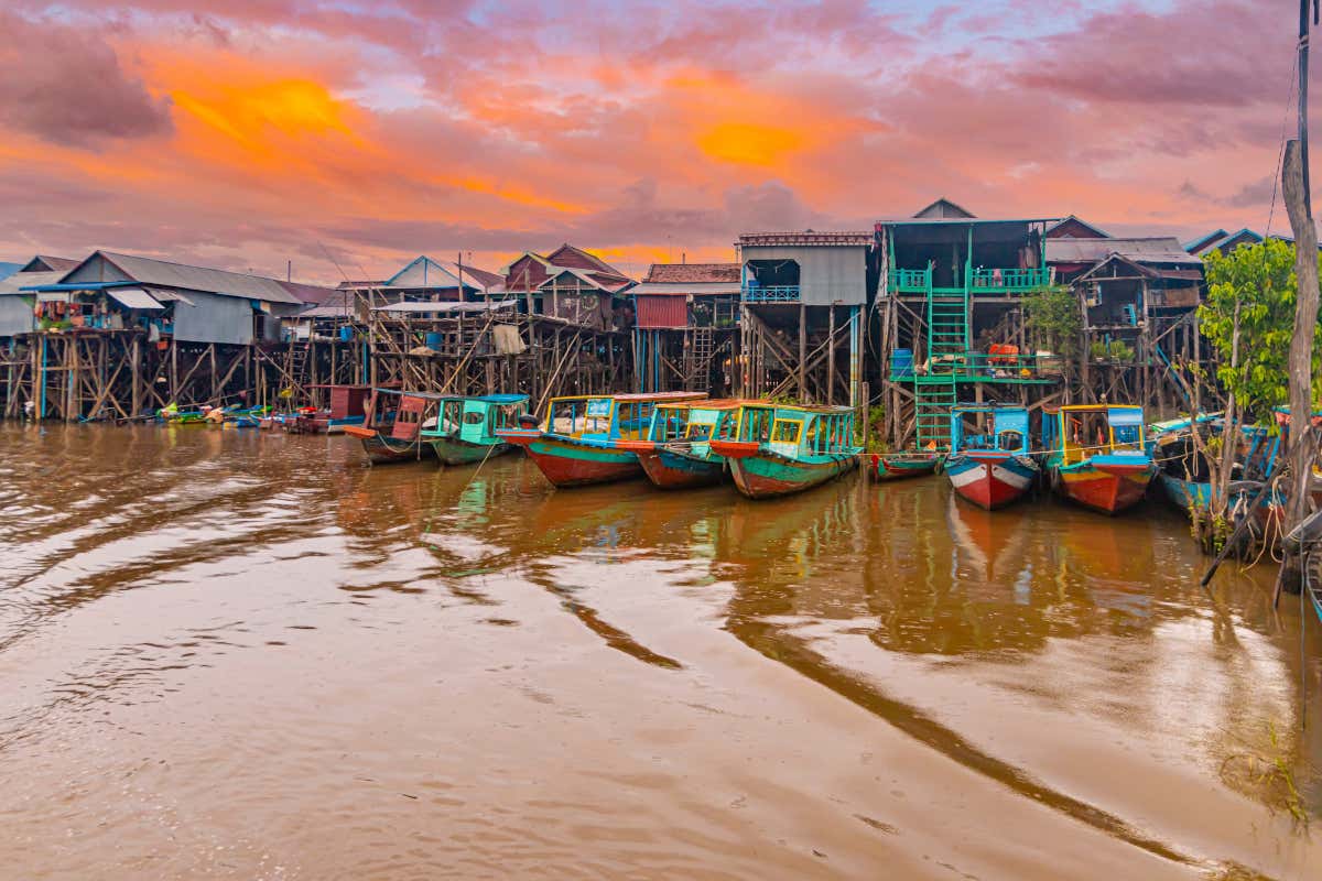 Coucher du soleil sur le lac Tonlé Sap et ses maisons sur pilotis, avec des barques colorées au premier plan