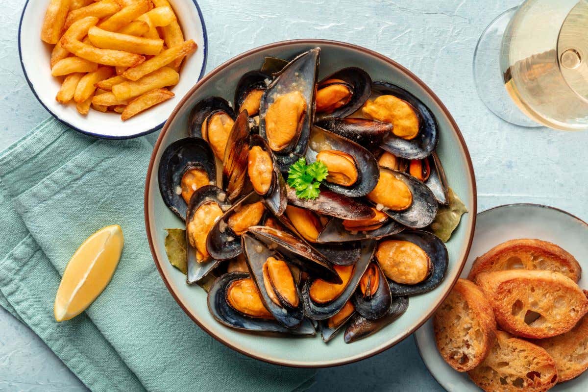 Un plato con mejillones junto a otro con patatas y pan