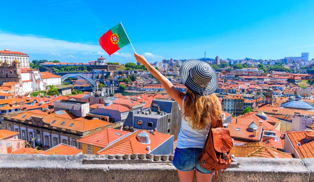 Chica sujetando una bandera de Portugal disfruta de la panorámica de la ciudad de Oporto