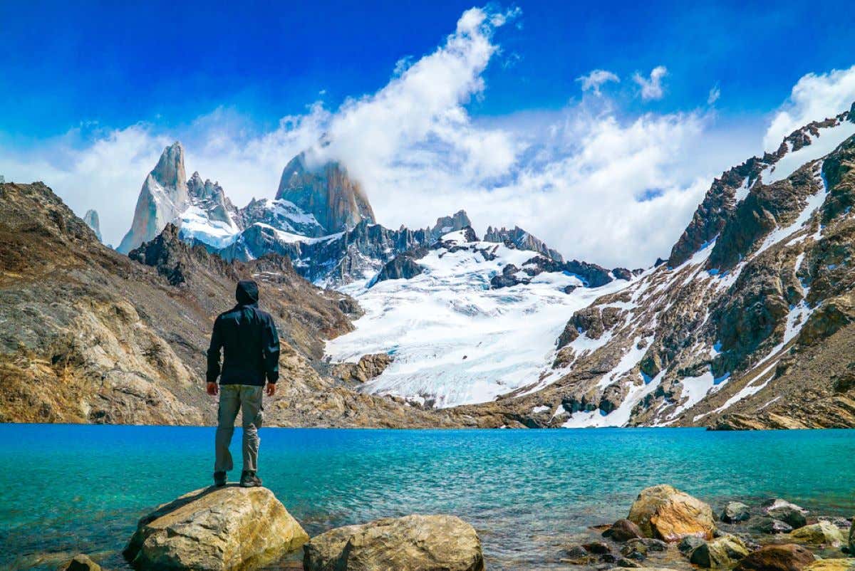A person standing on a rock with a lake and Mount Fitz Roy in the distance.