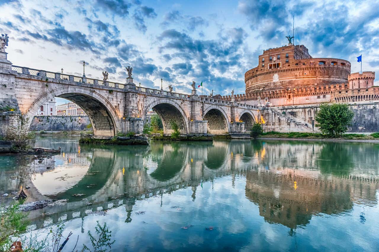 Castel Sant'Angelo visto dal Tevere con Ponte Sant'Angelo e statue sotto un cielo nuvoloso