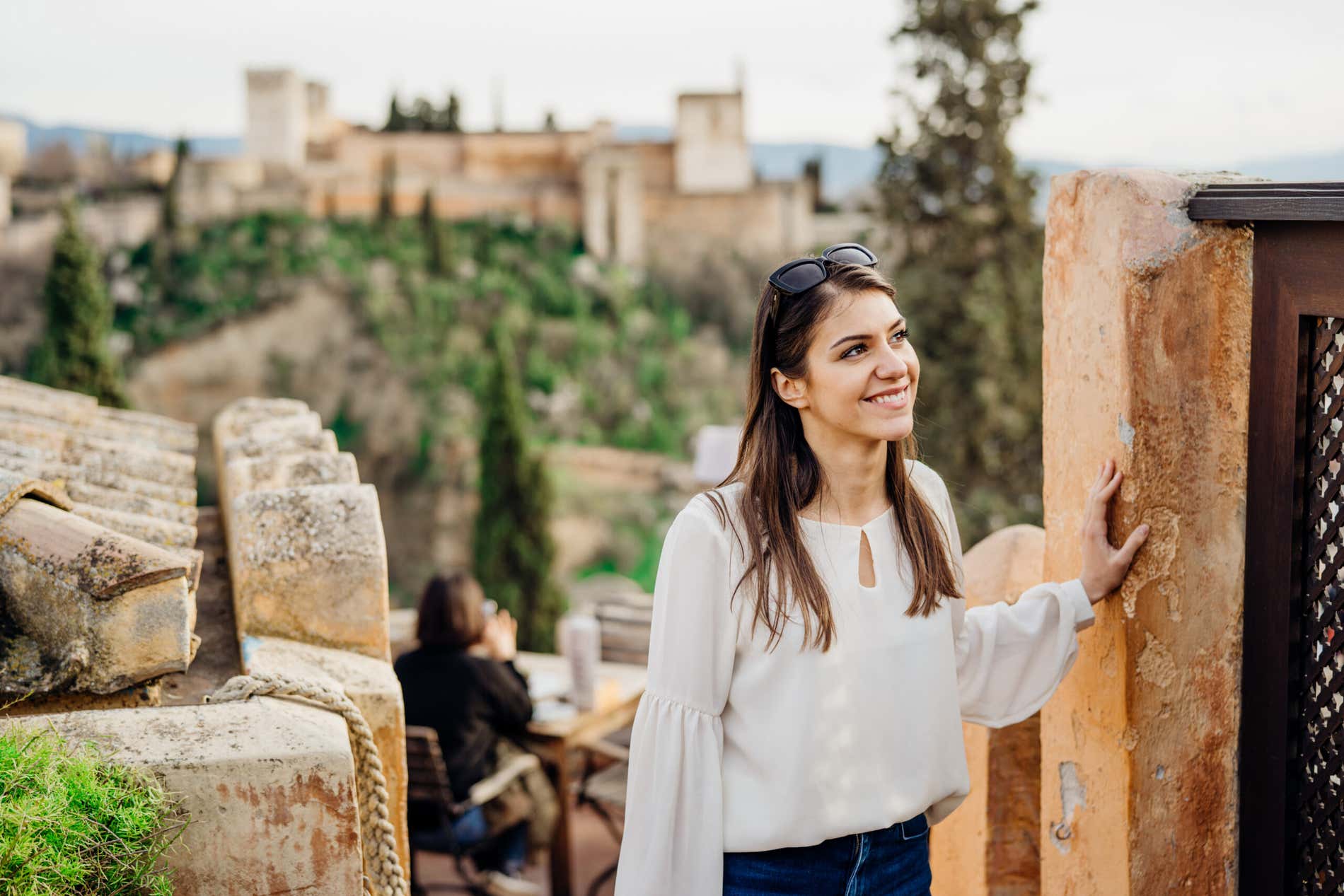 Una ragazza sorridente si appoggia a un muro mentre sale delle scale con l'Alhambra di Granada sullo sfondo