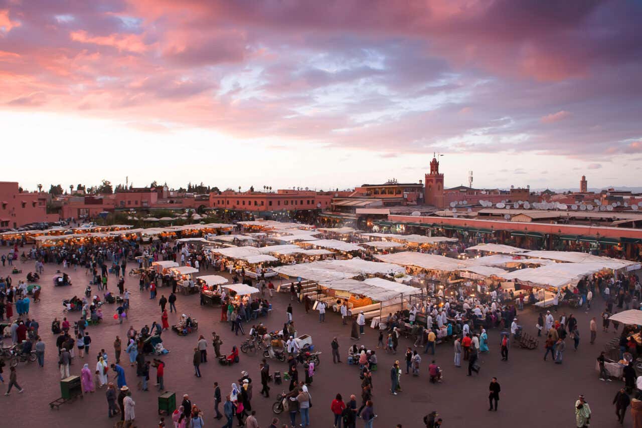 Panoramica della Piazza Jamaa el Fna al tramonto con bancarelle illuminate e persone che camminano