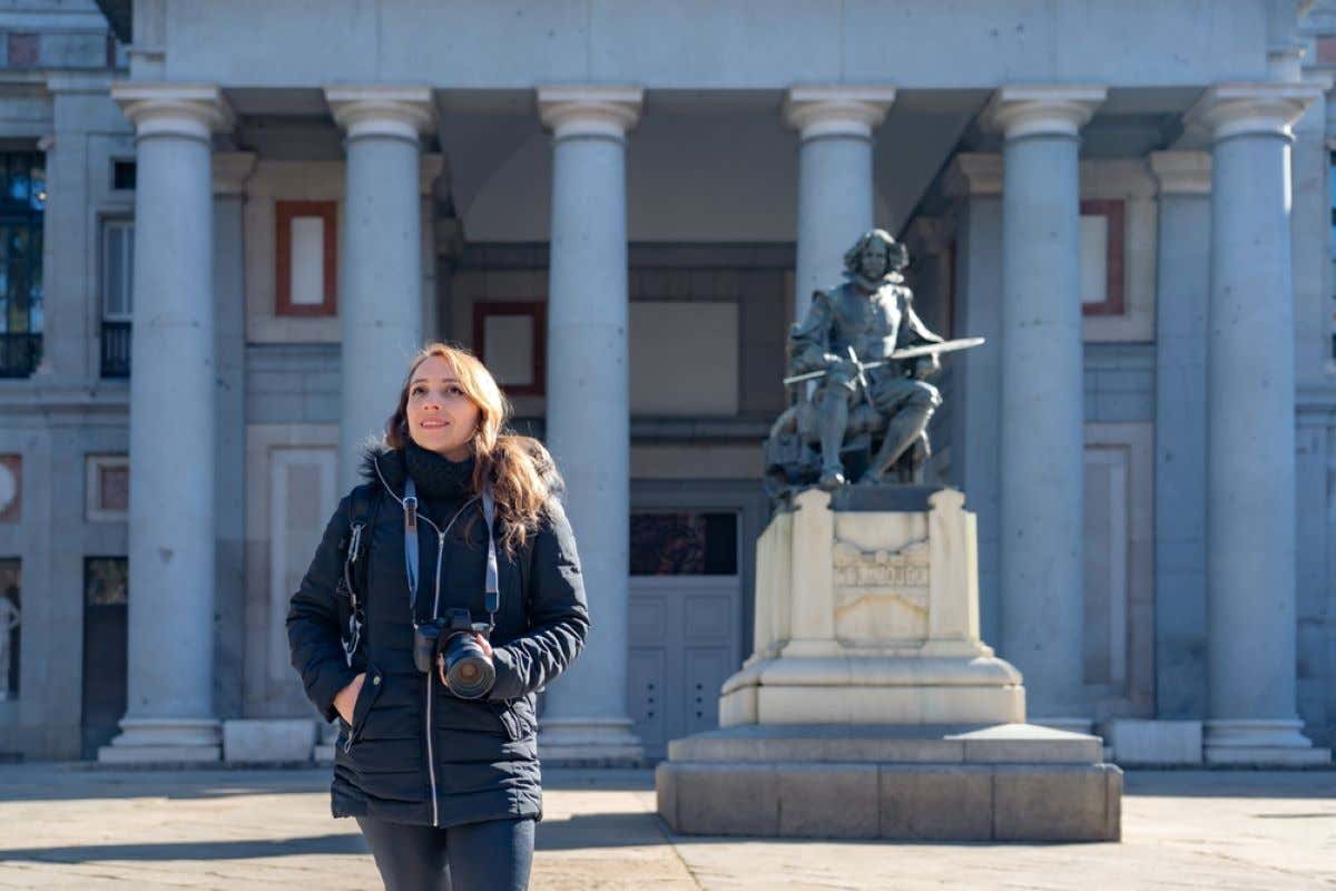 A woman standing in front of the statue of Diego Velázquez, located in front of the Museo del Prado.