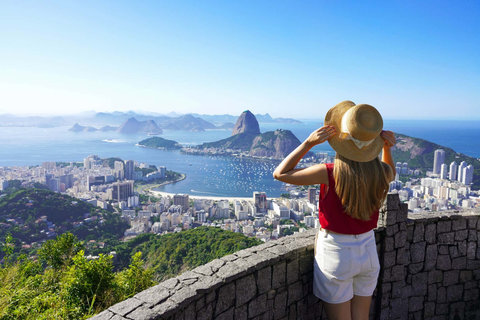 magem de uma turista vista de costas, apreciando a vista da famosa Baía de Guanabara com o Pão de Açúcar no Rio de Janeiro