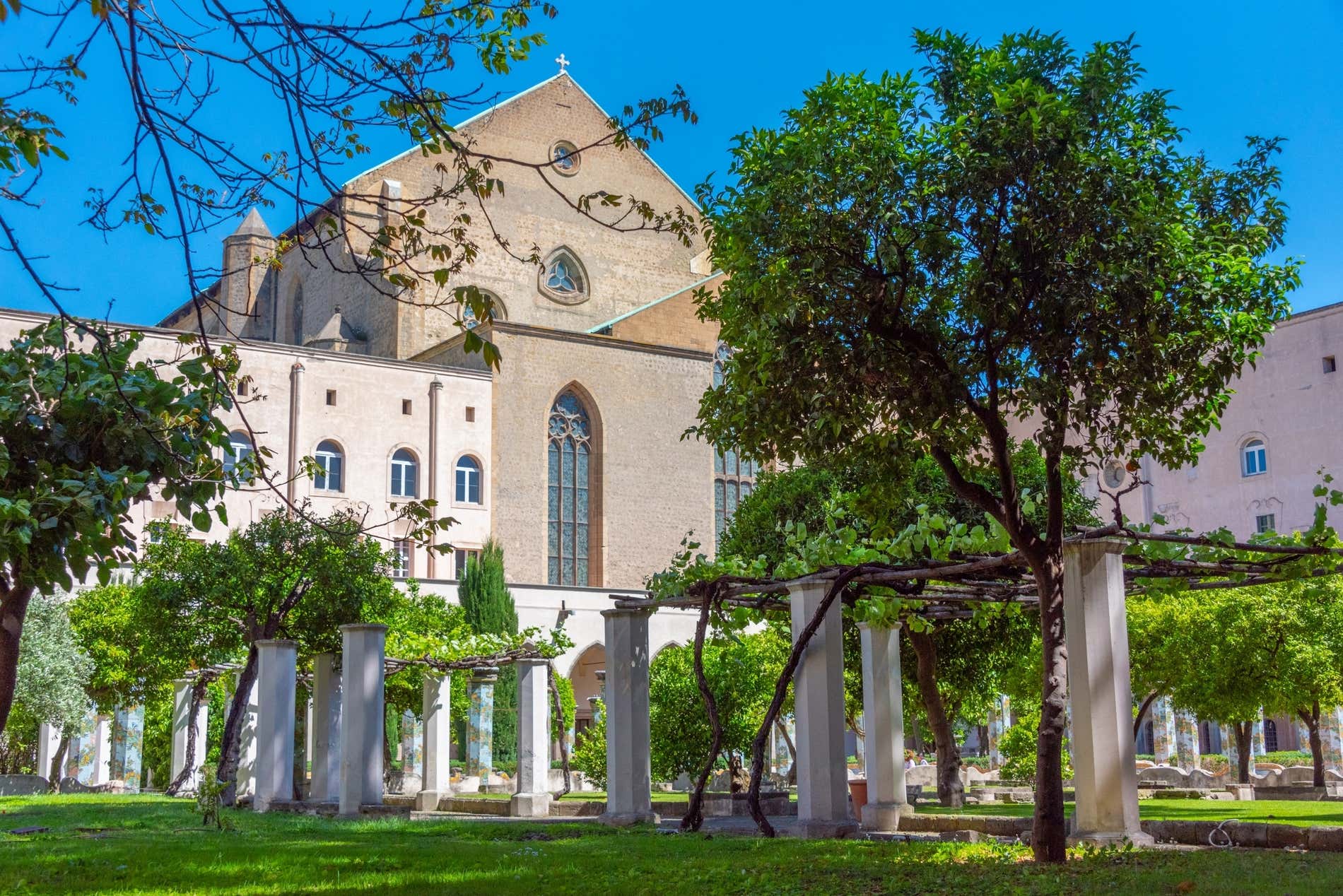 Un chiostro con colonne e alberi e una chiesa in secondo piano
