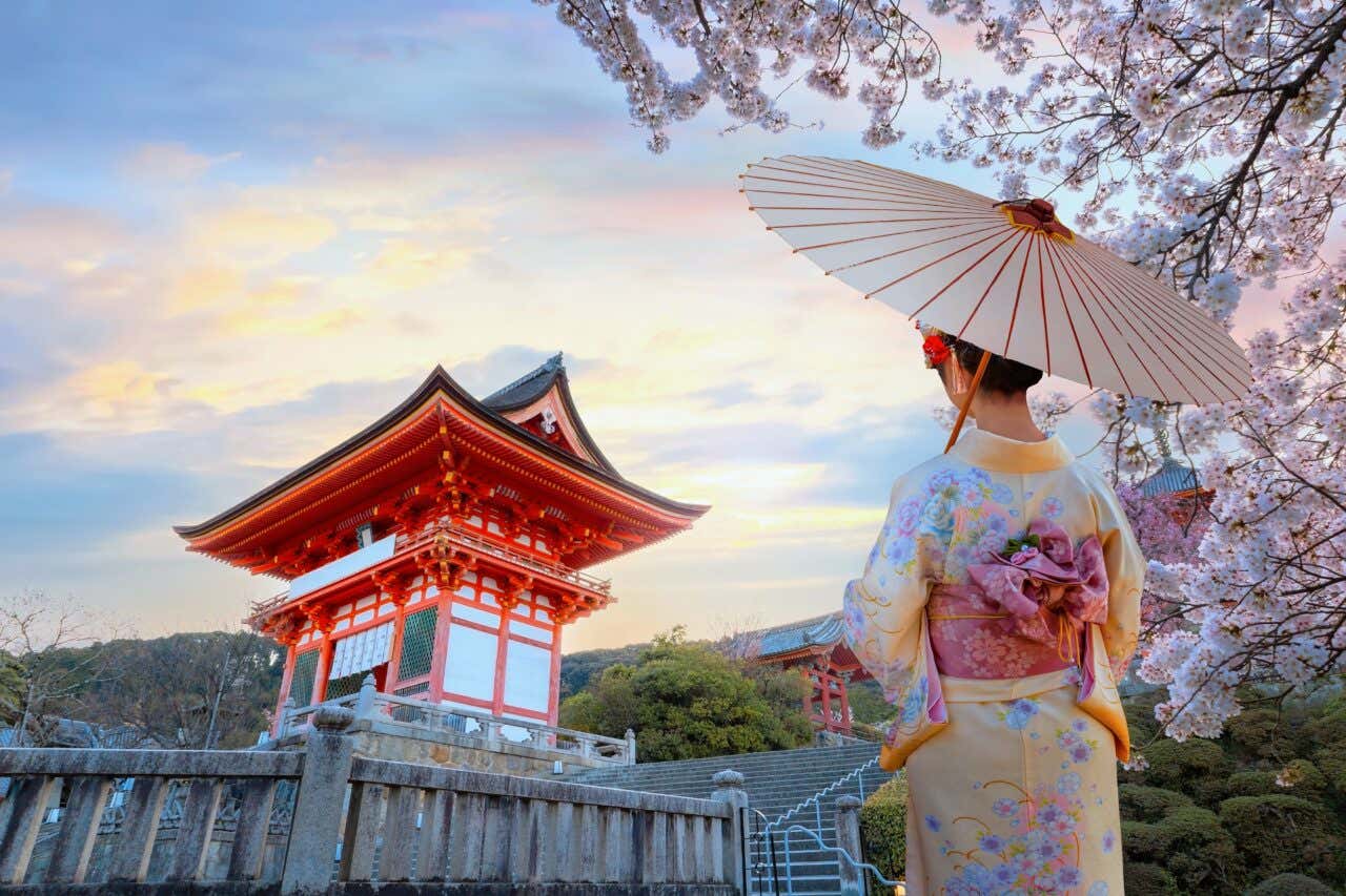 Femme japonaise en tenue traditionnelle à côté d'un cerisier en fleurs face au temple Kiyomizu