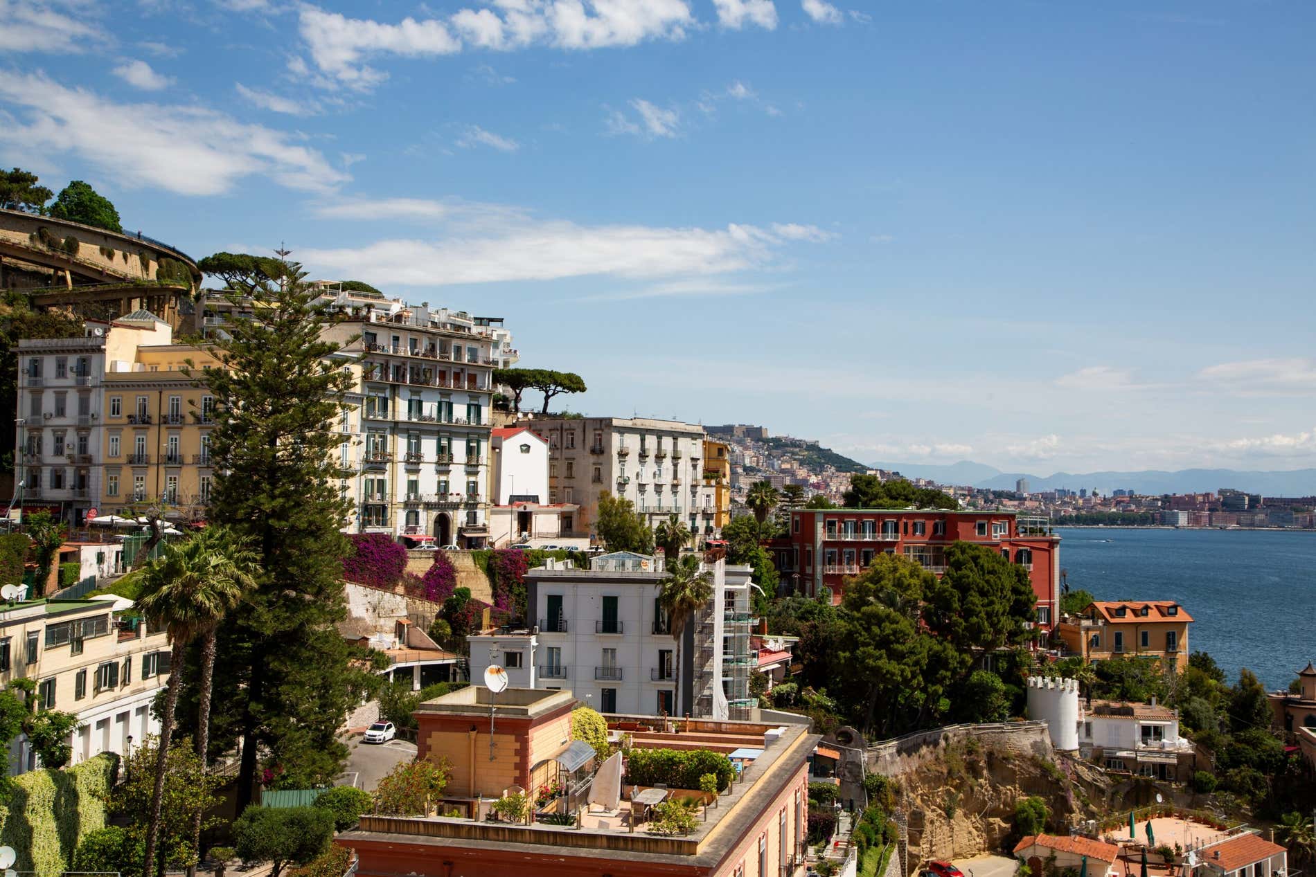 Scorcio della collina di Posillipo con alcuni alberi fra i palazzi e un angolo di mare