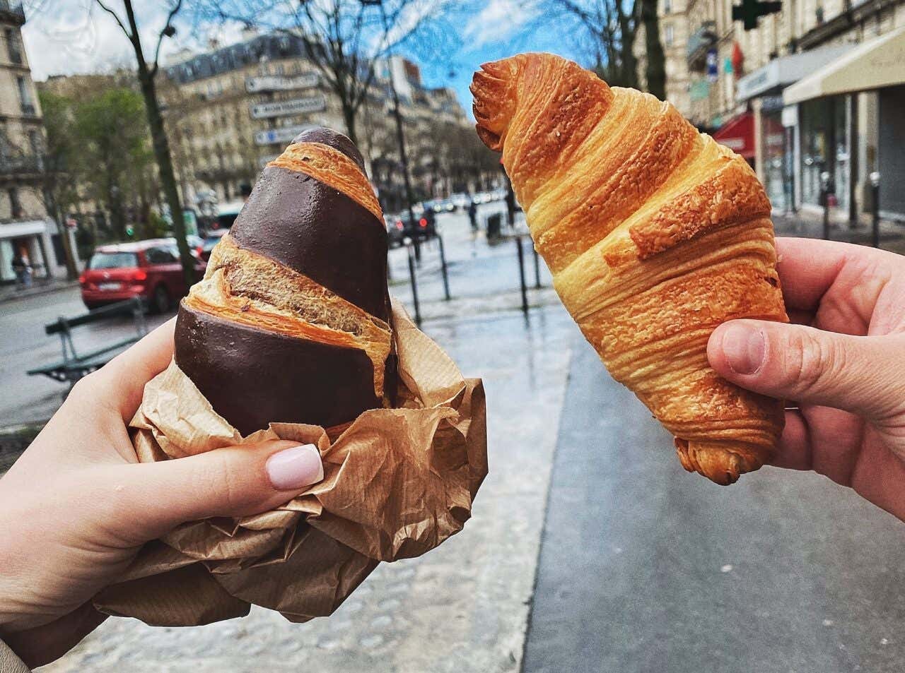 Duas mãos segurando croissants nas ruas de Paris