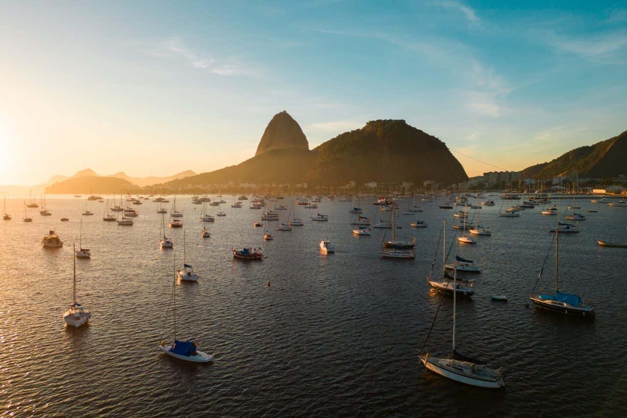 Muitos barcos pequenos na Baía de Botafogo, com o Pão de Açúcar no horizonte, ao nascer do sol no Rio de Janeiro