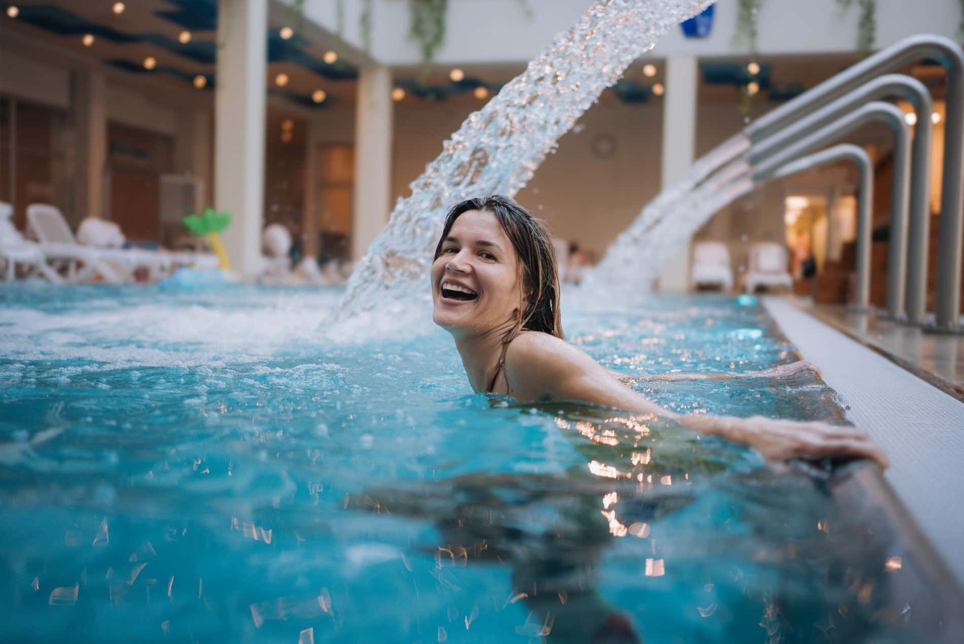 Una ragazza sorridente sotto un getto d'acqua in una piscina termale