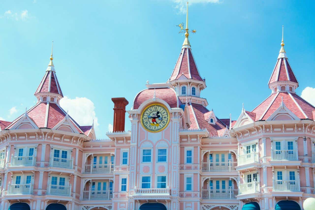 A pink castle in Disneyland Paris with a Mickey Mouse clock in the middle.
