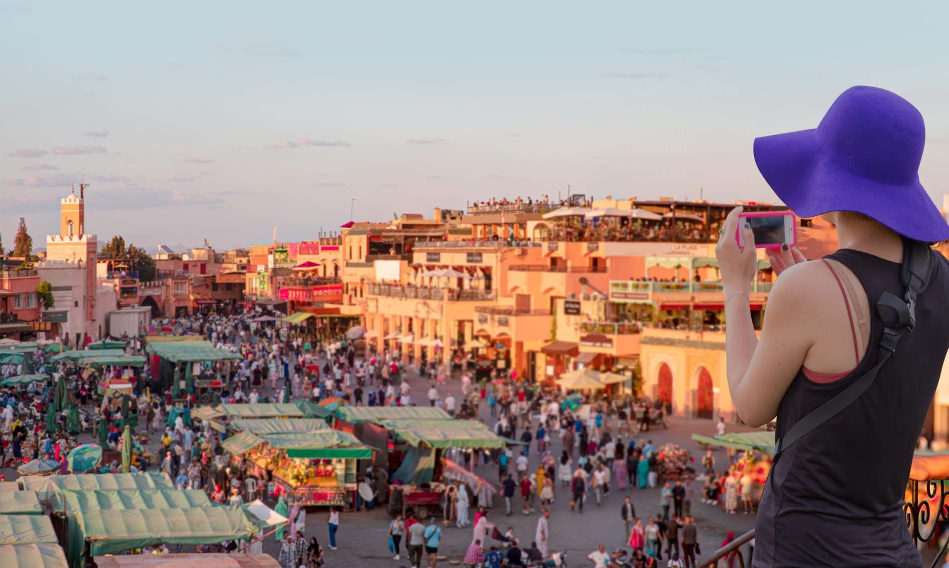 Una turista fotografa la piazza Jemma el Fna al tramonto con il suo cellulare da una terrazza