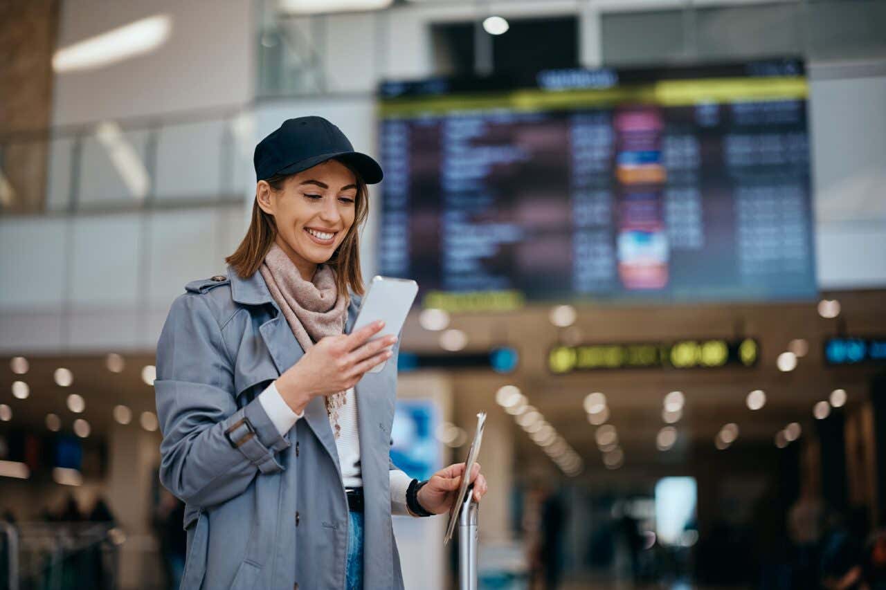 Una ragazza guarda il cellulare davanti a un maxi schermo dell'aeroporto
